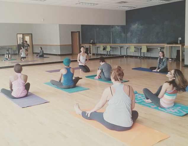 A dance studio full of people on yoga mats practicing yoga.