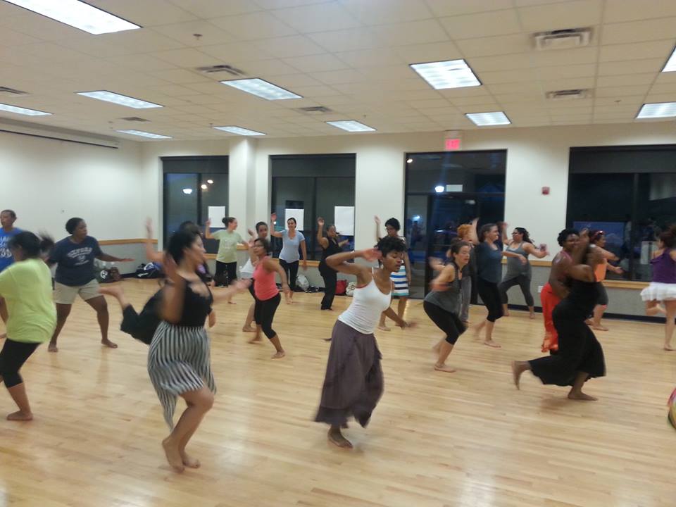 A dance studio full of people of all races and ages in an Afro Cuban dance class with live drumming.