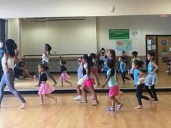 Three young girls, one in a pink tutu, another in a multicolor tutu and the other in workout clothing, are all practicing dance moves.