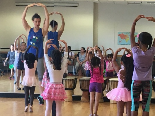 A children's ballet class with a diverse studio of children practicing piles.