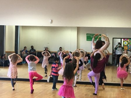 A room full of young boys and girls looking in a dance studio mirror as they practice ballet.